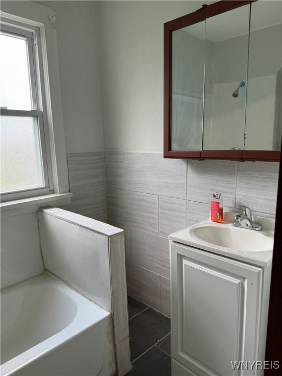 bathroom with a tub to relax in, vanity, tile walls, and a healthy amount of sunlight