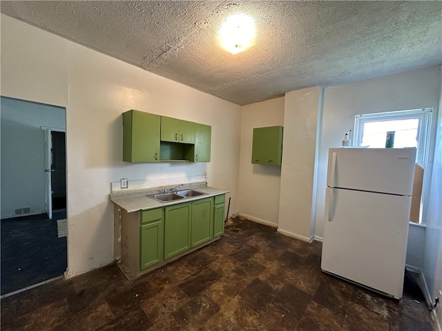 kitchen featuring a textured ceiling, green cabinetry, white refrigerator, and sink