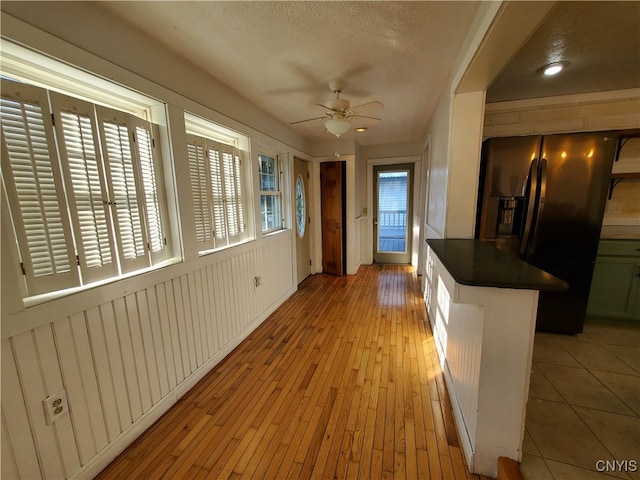 kitchen featuring a textured ceiling, black fridge with ice dispenser, ceiling fan, and light hardwood / wood-style floors