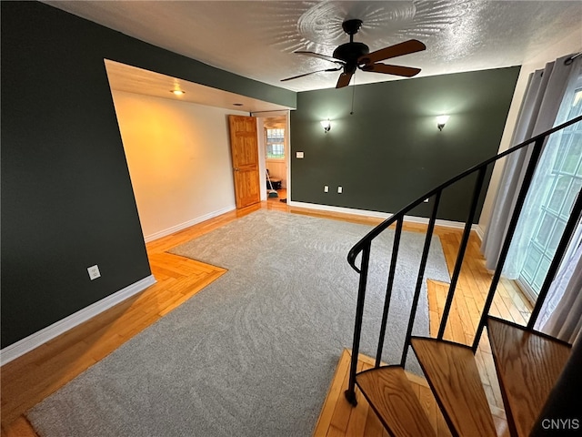 staircase with a textured ceiling, ceiling fan, and hardwood / wood-style flooring