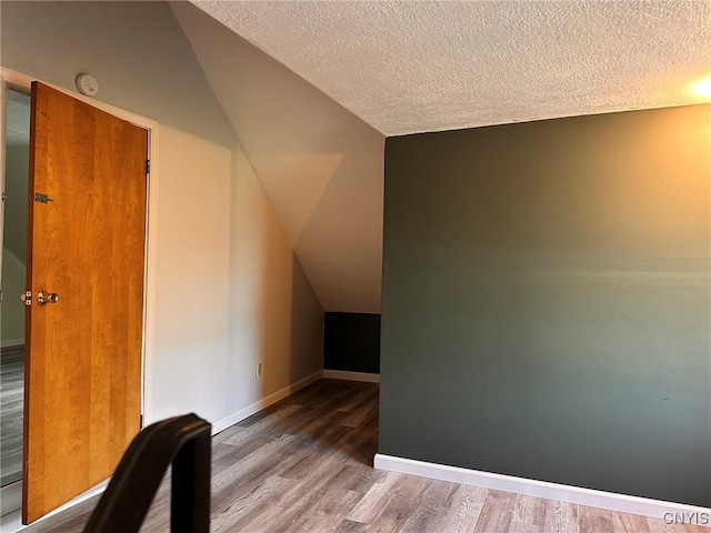 additional living space featuring vaulted ceiling, a textured ceiling, and hardwood / wood-style floors