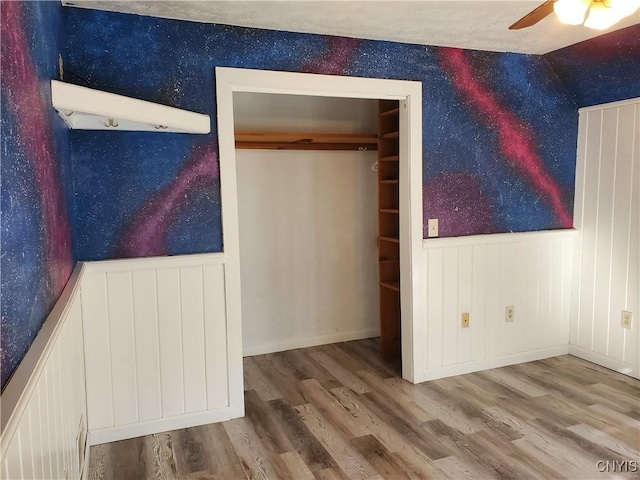 205 S James St, Wilna, NY 13619 - unfurnished bedroom with wallpapered walls, wood finished floors, a wainscoted wall, and ceiling fan