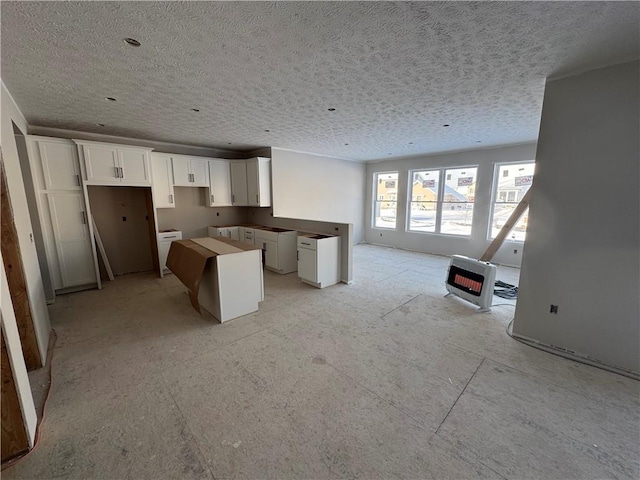 kitchen featuring heating unit, a kitchen island, a textured ceiling, and white cabinets