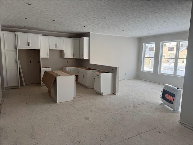 kitchen with white cabinetry, a center island, heating unit, and a textured ceiling