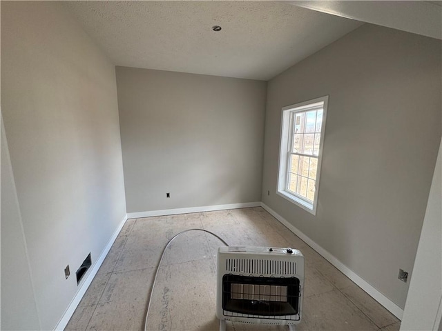unfurnished room with heating unit, a textured ceiling, and baseboards
