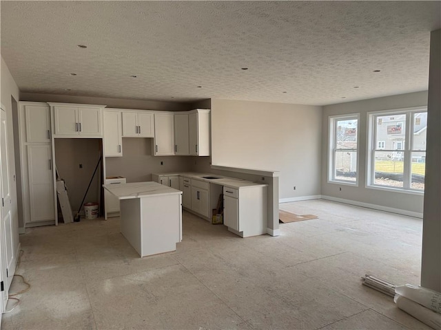kitchen with a textured ceiling, white cabinetry, a kitchen island, and baseboards