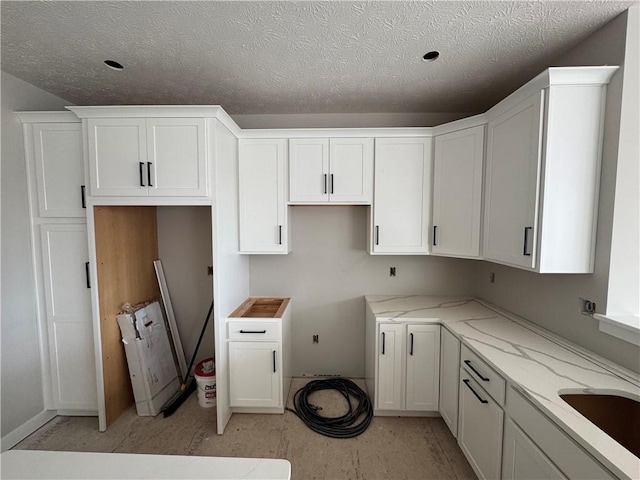 kitchen with light stone counters, a textured ceiling, white cabinets, and a sink