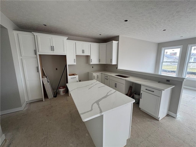 kitchen with light stone counters, baseboards, a kitchen island, a peninsula, and white cabinetry