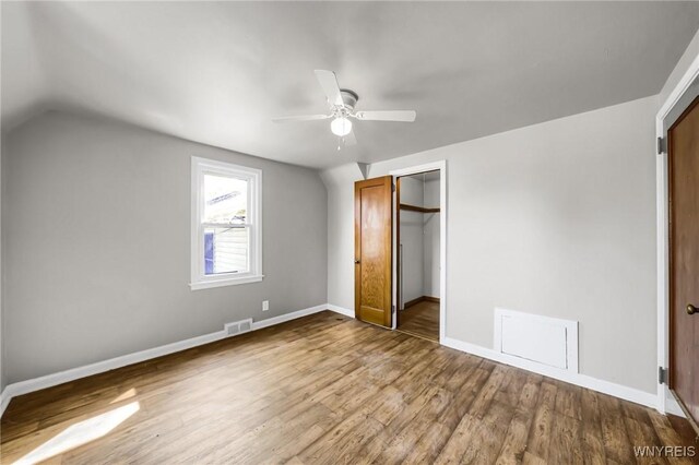 unfurnished bedroom featuring vaulted ceiling, hardwood / wood-style floors, a walk in closet, a closet, and ceiling fan