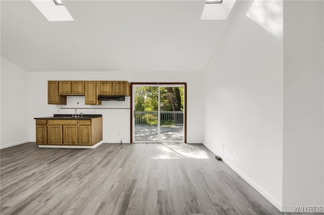 kitchen featuring vaulted ceiling with skylight, sink, and light hardwood / wood-style flooring