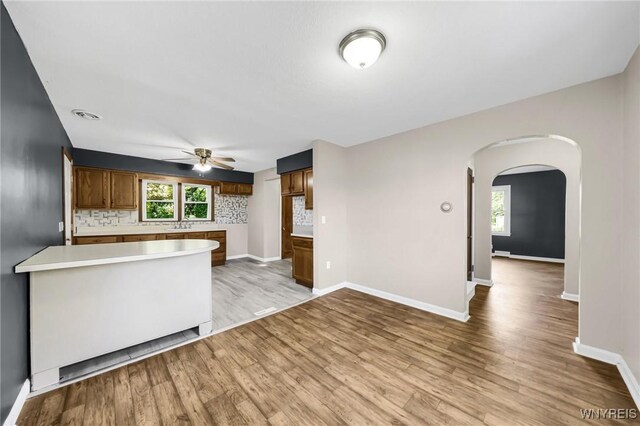 kitchen featuring light hardwood / wood-style flooring, backsplash, kitchen peninsula, and ceiling fan