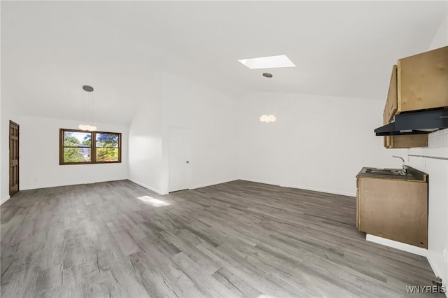 unfurnished living room featuring an inviting chandelier, vaulted ceiling with skylight, hardwood / wood-style flooring, and sink