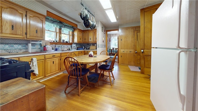 kitchen with black gas stove, white fridge, backsplash, and light hardwood / wood-style floors