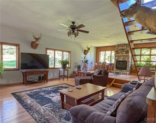 living room with light hardwood / wood-style flooring, ceiling fan, a wealth of natural light, and a stone fireplace