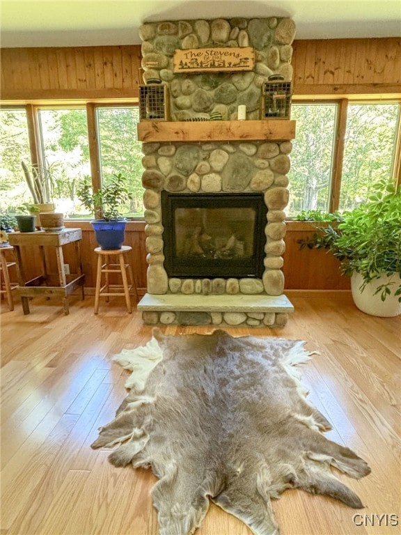 living room with hardwood / wood-style flooring, wooden walls, and a stone fireplace