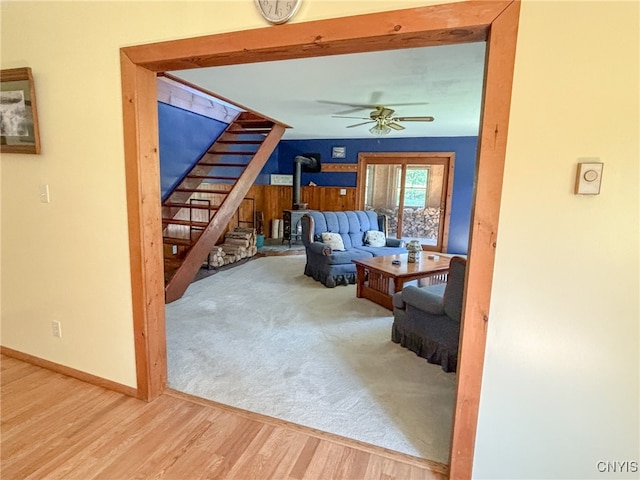 living room with hardwood / wood-style floors, ceiling fan, and a wood stove