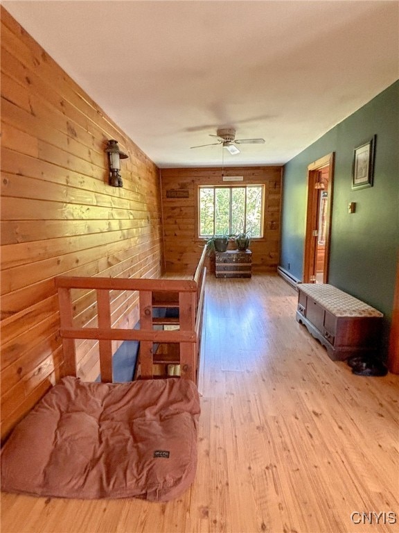 interior space with ceiling fan, light wood-type flooring, and wooden walls