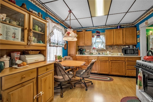 kitchen with pendant lighting, light hardwood / wood-style floors, white gas range oven, and a drop ceiling