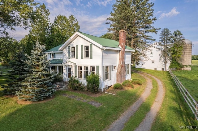 view of front facade with driveway, a chimney, a front yard, and fence