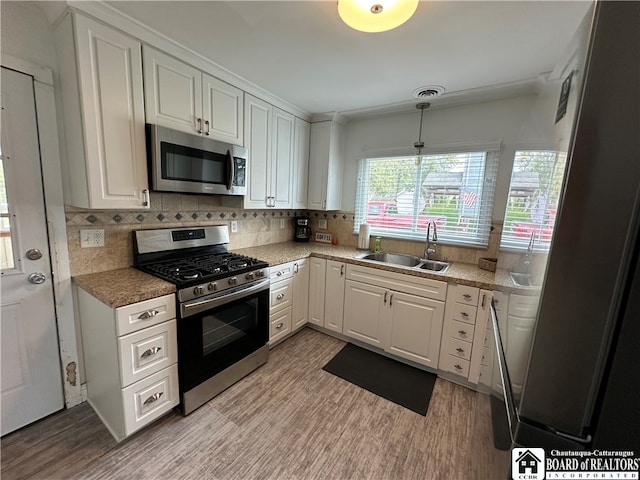 kitchen with white cabinets, backsplash, stainless steel appliances, light hardwood / wood-style floors, and sink