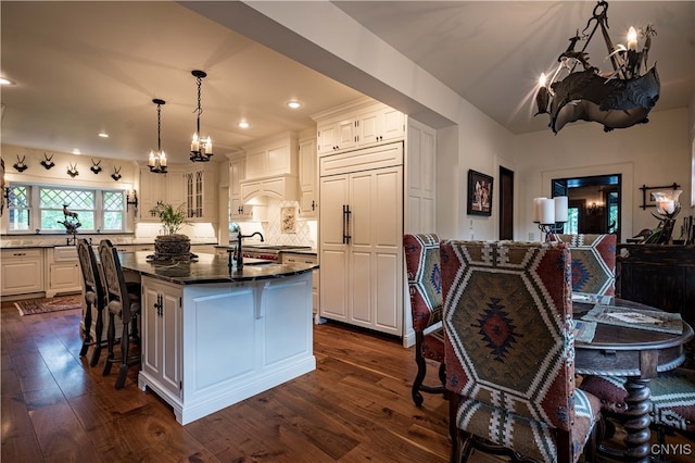 kitchen with a breakfast bar area, dark hardwood / wood-style flooring, an island with sink, white cabinetry, and paneled built in refrigerator