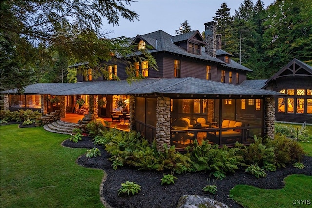 back house at dusk featuring a lawn and a sunroom