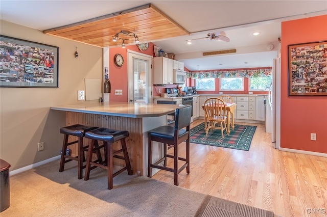 kitchen with light wood-type flooring, a breakfast bar area, white cabinetry, kitchen peninsula, and white appliances