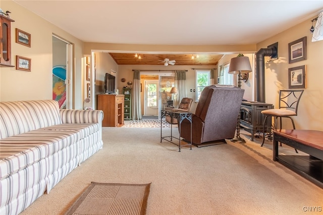 carpeted living room with a wood stove, ceiling fan, and beamed ceiling