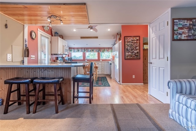 kitchen with light wood-type flooring, white cabinets, kitchen peninsula, a kitchen breakfast bar, and white appliances