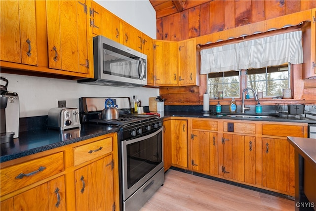 kitchen with wooden walls, stainless steel appliances, sink, and light hardwood / wood-style flooring