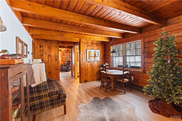 dining room featuring light wood-type flooring, wood ceiling, beamed ceiling, and wood walls