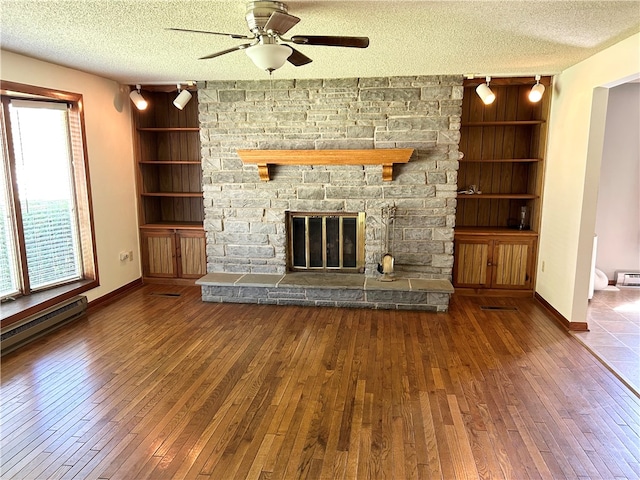 unfurnished living room with a textured ceiling, ceiling fan, a stone fireplace, and hardwood / wood-style flooring