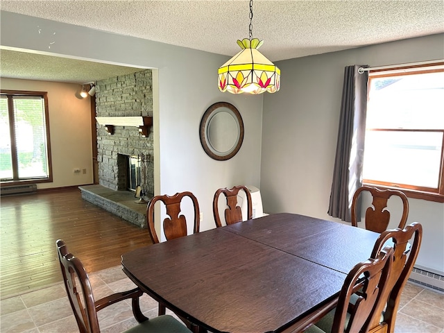 dining area with a stone fireplace, a healthy amount of sunlight, hardwood / wood-style floors, and a textured ceiling