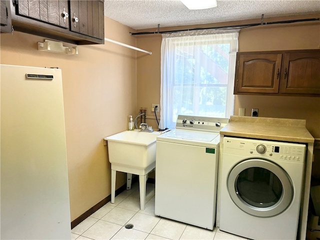 laundry room with light tile patterned floors, a textured ceiling, cabinets, and washer and clothes dryer