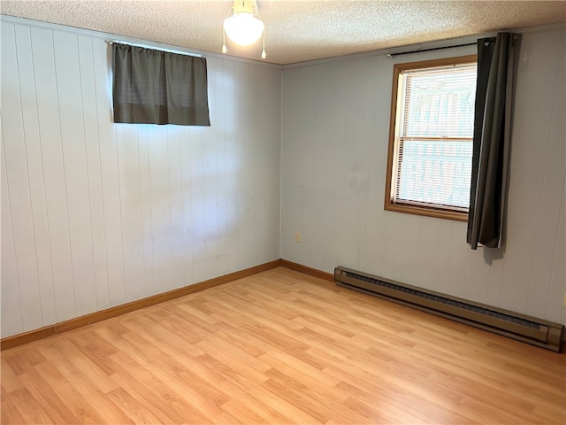 unfurnished room featuring wood walls, baseboard heating, a textured ceiling, and light hardwood / wood-style flooring