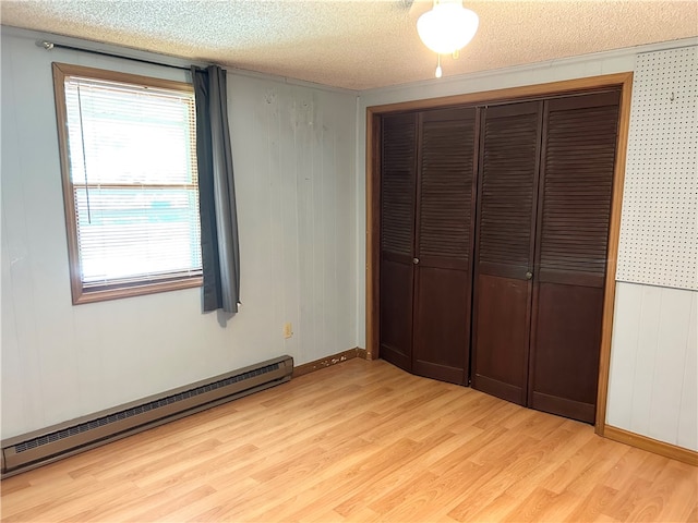 unfurnished bedroom with a baseboard heating unit, light hardwood / wood-style flooring, a closet, and multiple windows