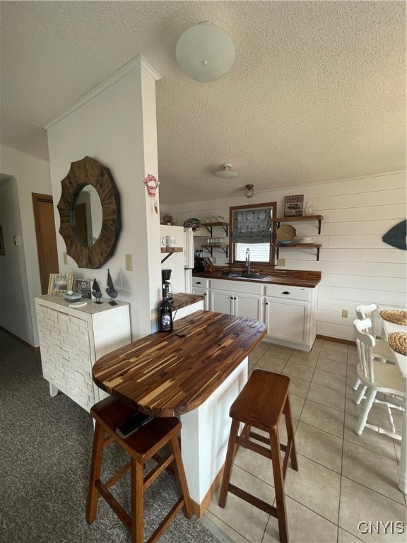 dining room featuring a textured ceiling, light tile patterned flooring, wooden walls, and sink