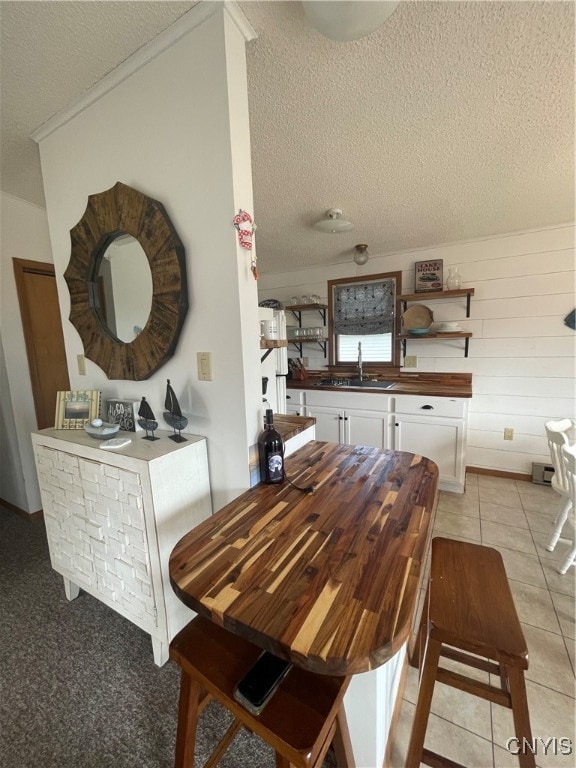 tiled dining space with ornamental molding, a textured ceiling, wooden walls, and sink