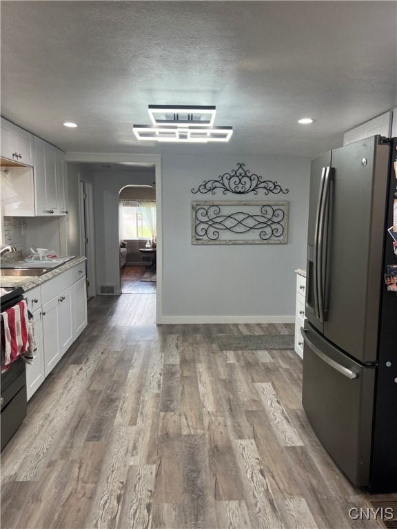 kitchen with stainless steel fridge with ice dispenser, light wood-type flooring, white cabinetry, and sink