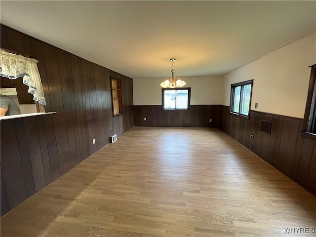 empty room featuring wood walls, a notable chandelier, and light wood-type flooring