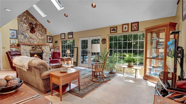 carpeted living room featuring high vaulted ceiling, a skylight, french doors, and a stone fireplace