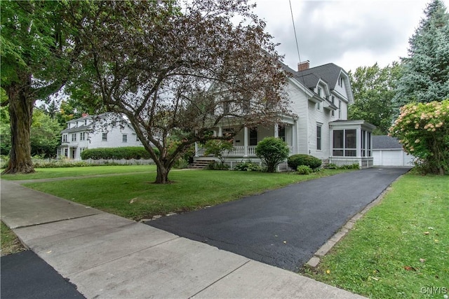 view of front facade featuring a garage, covered porch, a chimney, and a front yard