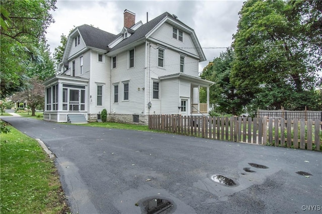 exterior space featuring roof with shingles, a fenced front yard, a sunroom, and a chimney