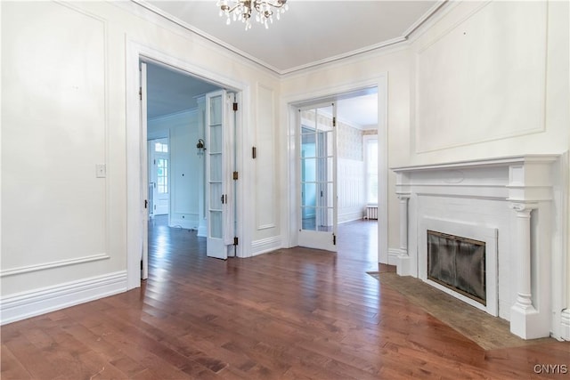 unfurnished living room with a glass covered fireplace, crown molding, a notable chandelier, and wood finished floors