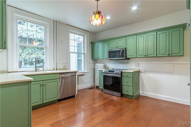 kitchen featuring light wood finished floors, green cabinetry, light countertops, stainless steel appliances, and a sink