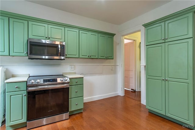 kitchen with wood finished floors, appliances with stainless steel finishes, light countertops, green cabinetry, and baseboards