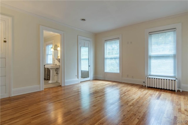 empty room featuring ornamental molding, a sink, wood finished floors, radiator, and baseboards