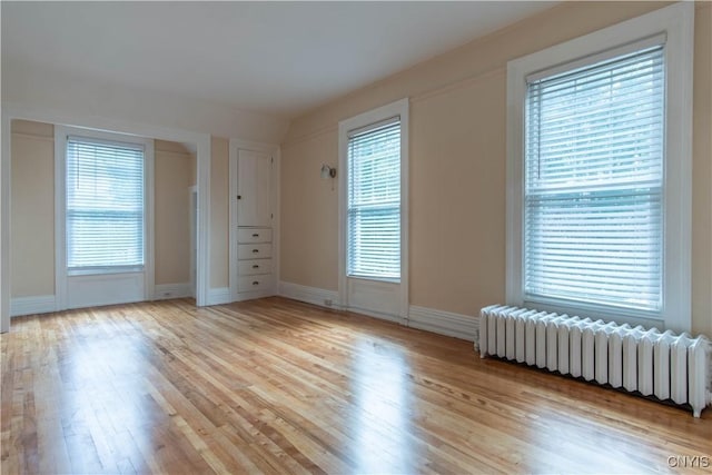 spare room with light wood-style flooring, radiator, baseboards, and a wealth of natural light