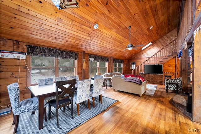 dining room featuring vaulted ceiling, light wood-type flooring, wood ceiling, wood walls, and ceiling fan