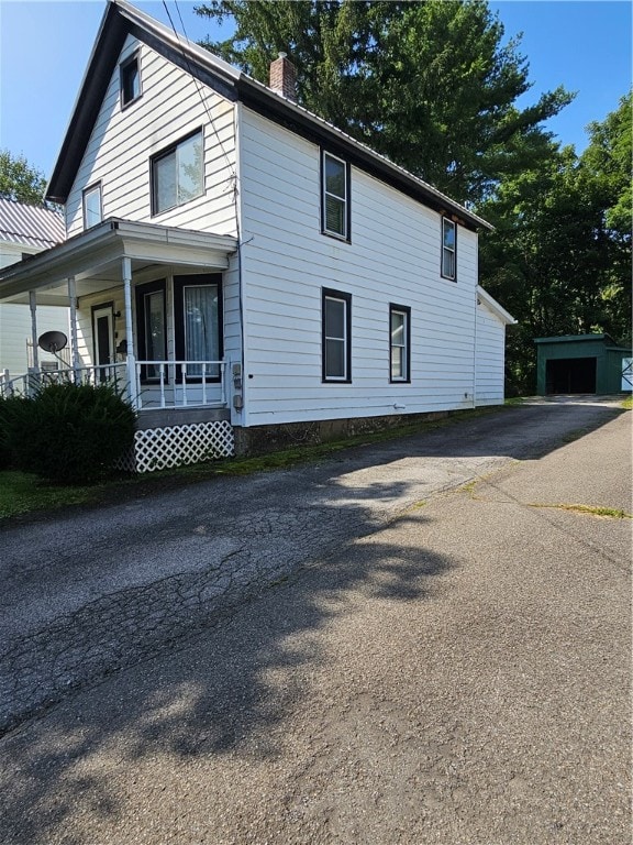 view of side of home featuring an outdoor structure, a garage, and a porch